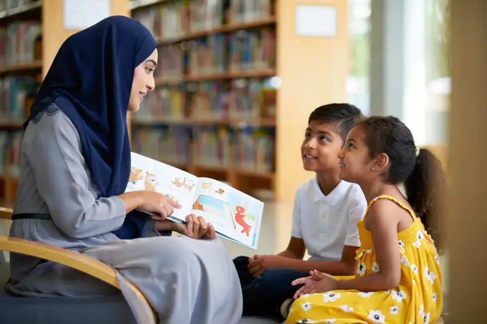 امرأة تُعلّم طفلَيها من خلال كتابٍ للأطفال، وهما يستمعان باهتمام