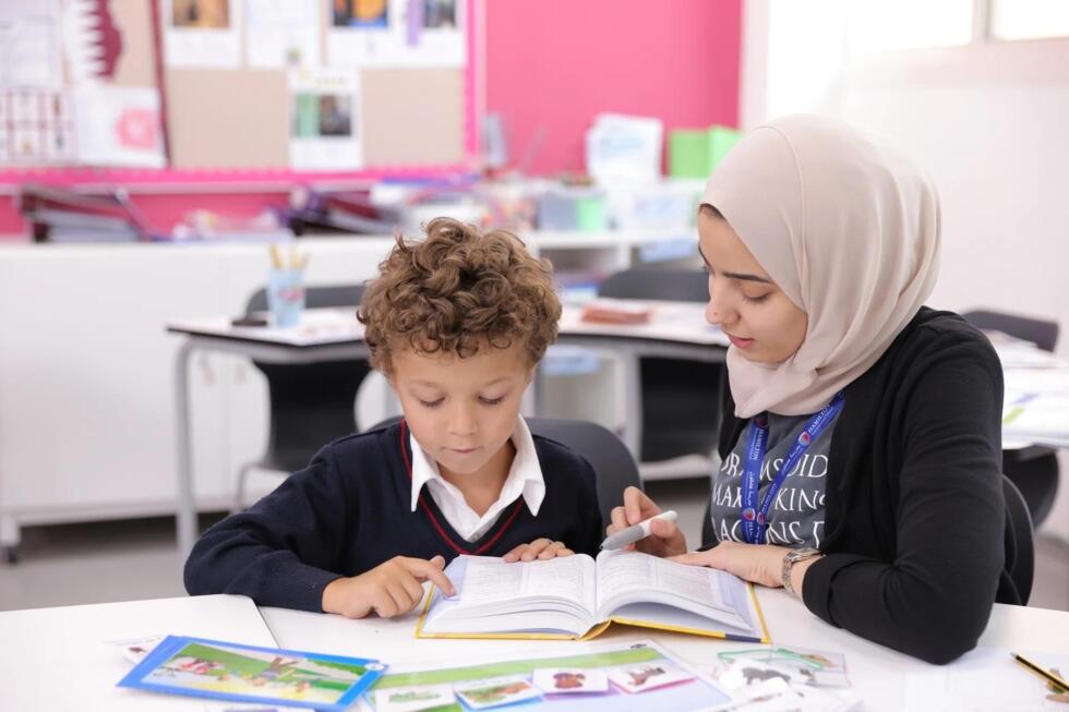 معلمة تساعد طالباً صغيراً في القراءة خلال جلسة دروس خصوصية فردية.