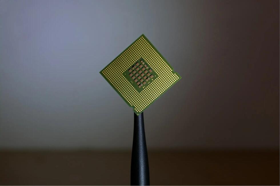 معالج كمبيوتر (CPU) مربع الشكل ومثبت بواسطة أداة التقاط، تظهر من جهته الخلفية مصفوفة من نقاط الاتصال الذهبية.